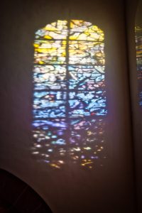 Colorful light from a stained glass window is projected onto a white wall, forming a blurred and vibrant reflection.
