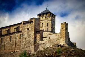 Stone castle with a central tower stands on a rocky hill under a partly cloudy sky.