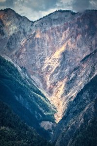 Steep, rocky mountain slopes with patches of green forest and sunlight illuminating the rugged terrain.